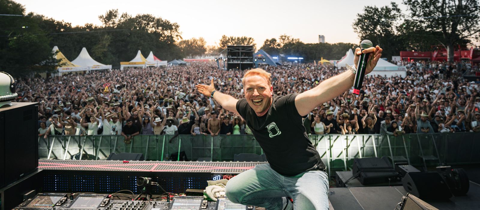 DJ auf der Bühne mit ausgebreiteten Armen vor vollem Festivalgelände